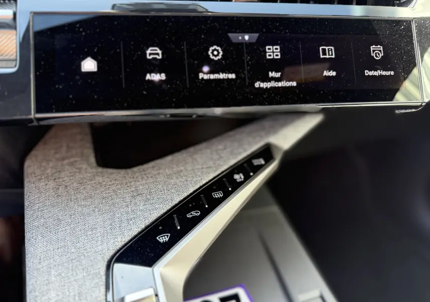 Gros plan sur la console centrale du Peugeot 5008 Hybrid 2025, avec écran tactile et commandes tactiles sur habillage gris clair.