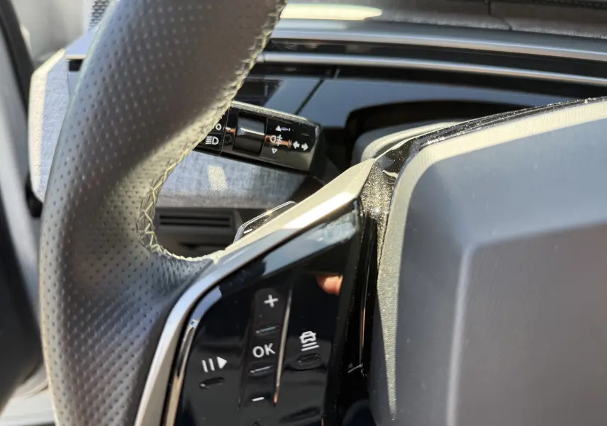Gros plan sur le volant perforé et les commandes multifonctions du Peugeot 5008 Hybrid 145 CH GT, intérieur moderne.