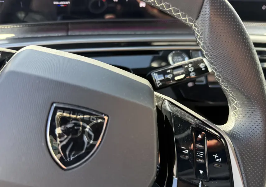 Gros plan sur le volant cuir perforé du Peugeot 5008 Hybrid 145 GT, avec commandes intégrées et logo lion central.