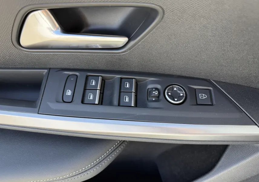 Gros plan sur la commande des vitres et rétroviseurs côté conducteur du Peugeot 5008 Hybrid blanc, intérieur noir.