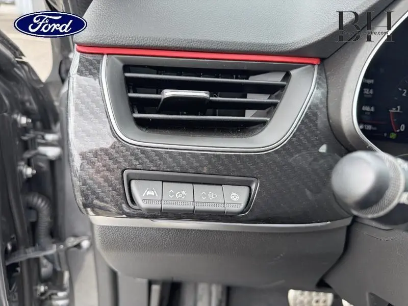 Détail intérieur côté gauche avec aérateur et commandes d'assistance sur tableau de bord noir et rouge.