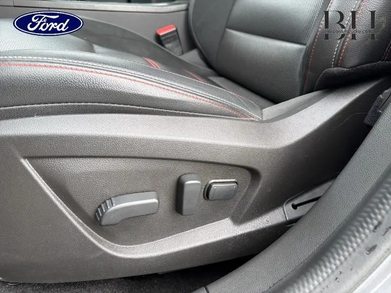 Détail du siège conducteur noir avec surpiqûres rouges et commandes électriques sur le côté droit.