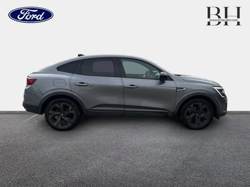 Profil droit d'un Renault Arkana gris métallisé 2023 avec jantes noires et lignes sportives marquées.