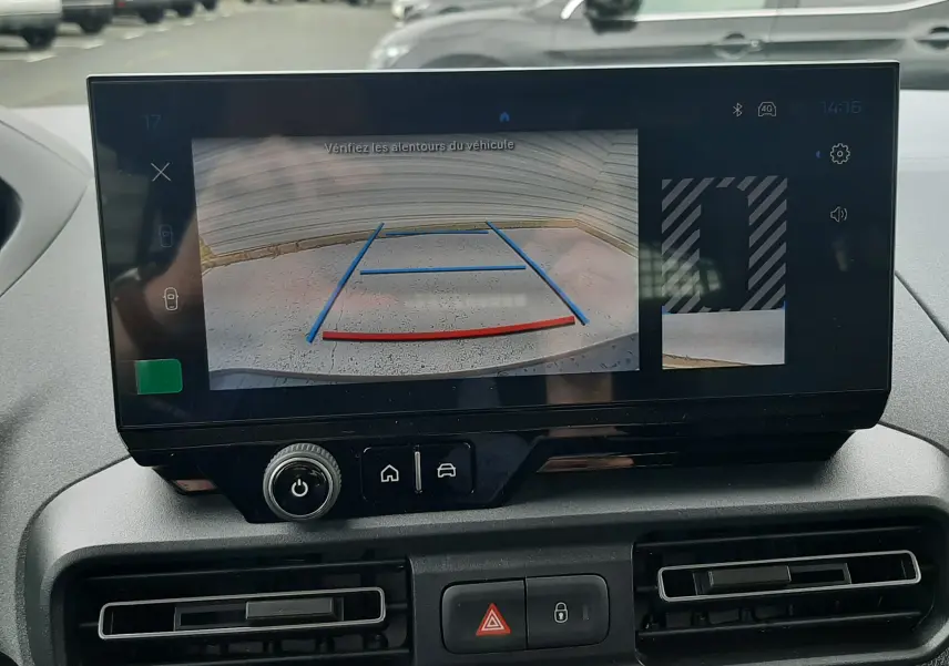 Écran central du Peugeot Rifter 2026 montrant la caméra de recul avec lignes de guidage, intérieur gris et commandes climatisation.
