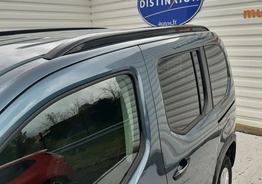 Vue 3/4 arrière côté droit du Peugeot Rifter bleu Kiama, mettant en valeur la galerie de toit et la vitre arrière teintée.