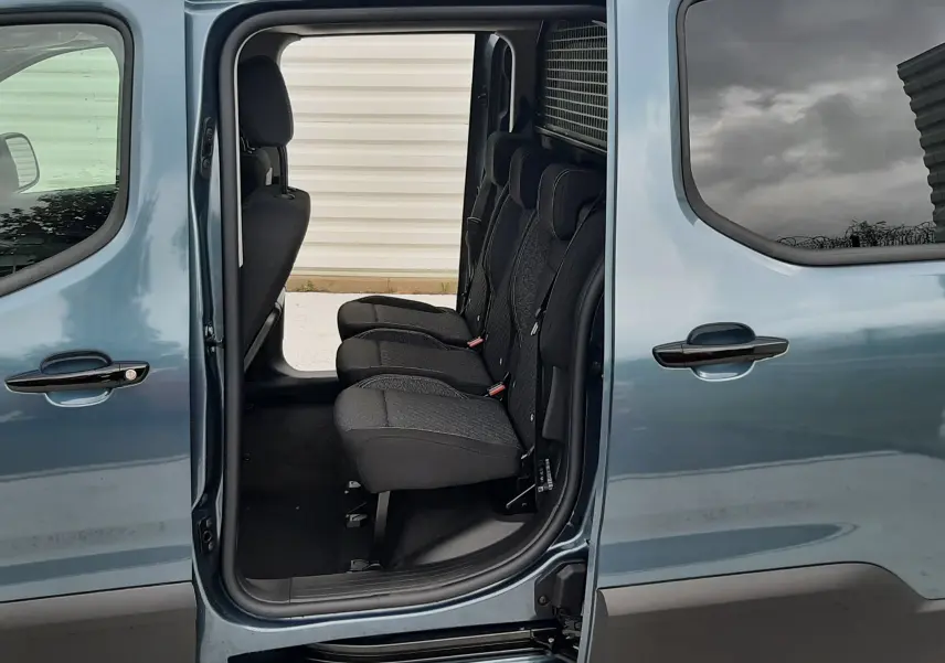 Vue latérale gauche du Peugeot Rifter bleu Kiama 2026 avec porte coulissante ouverte révélant les sièges arrière en tissu gris.