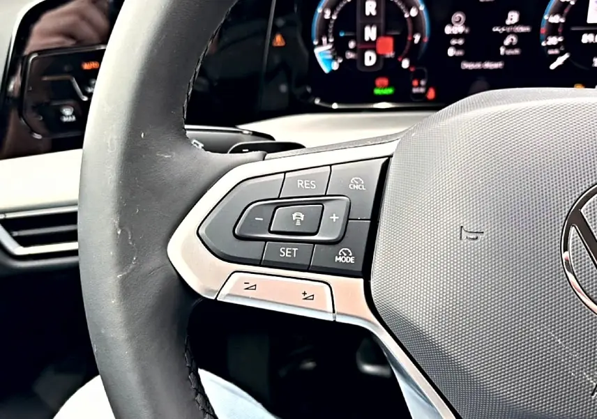Gros plan sur le volant noir de la Volkswagen Golf 2026, avec commandes intégrées et tableau de bord numérique en arrière-plan.