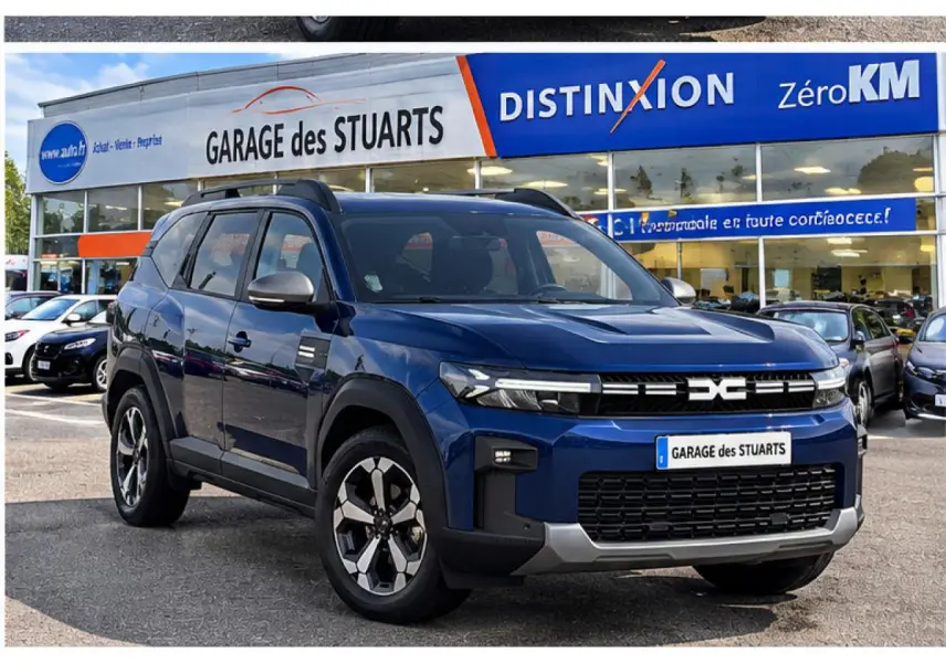 Dacia Bigster 2026 bleu indigo en 3/4 avant droit, avec jantes distinctives et toit noir, stationné devant un garage.