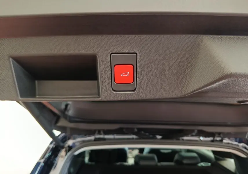 Bouton rouge d'ouverture électrique du coffre sur le hayon intérieur d'une Citroën C5 noire vue de l'arrière, coffre ouvert.