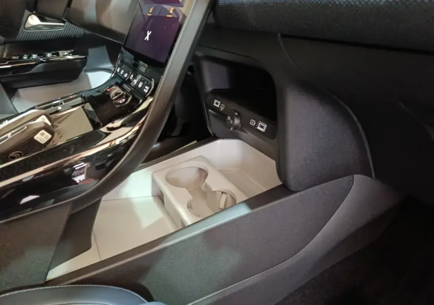 Intérieur de la Citroën C5 Hybride 2026, vue console centrale noire brillante avec porte-gobelets et prises USB.