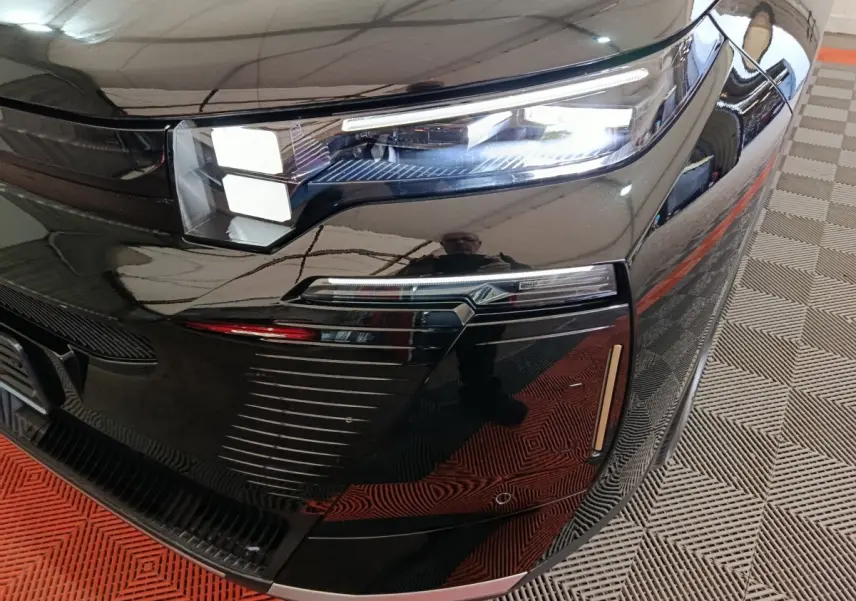 Gros plan sur le phare avant droit noir brillant du Citroën C5 Hybride 2026 avec éclairage LED et détails chromés.