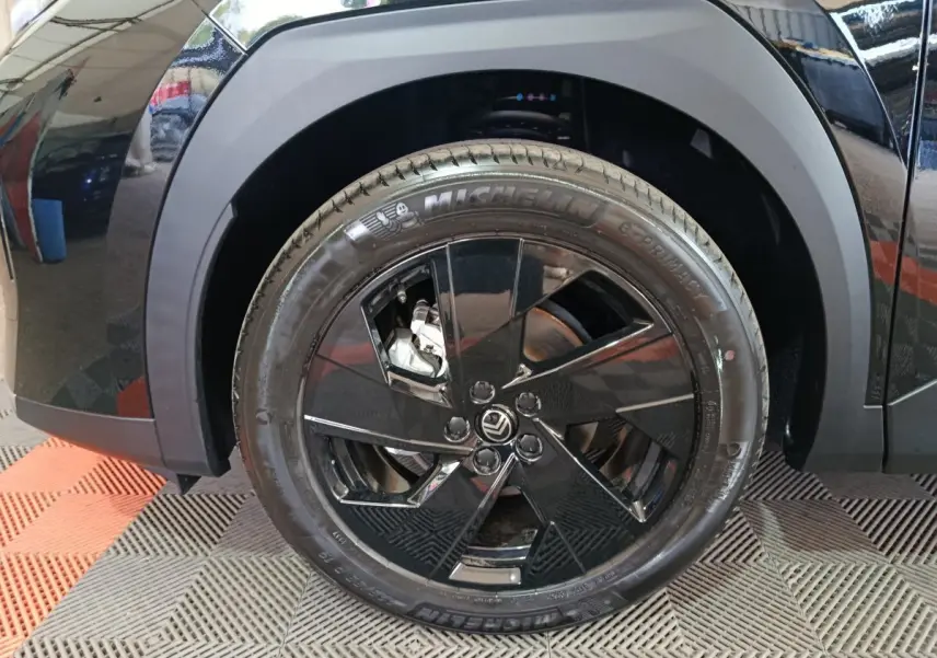 Gros plan sur la roue avant gauche noire avec jante noire brillante et logo Citroën visible sur une C5 hybride.