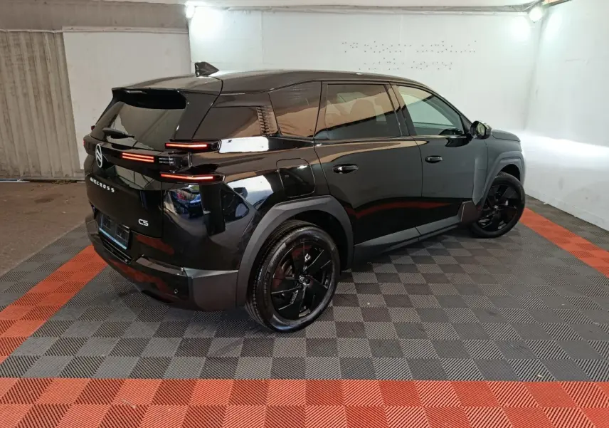 Vue 3/4 arrière droit d'une Citroën C5 noire avec feux arrière LED et jantes noires dans un garage.