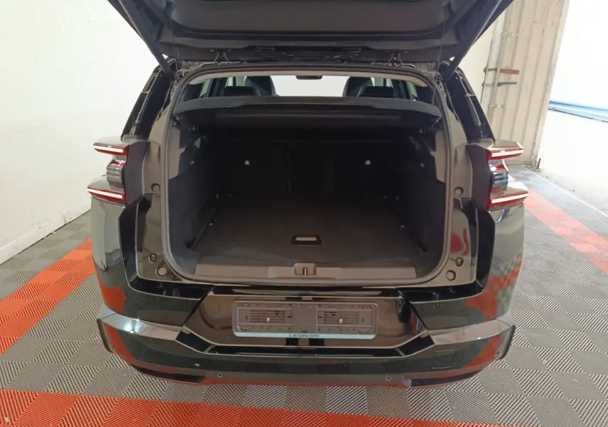 Vue arrière d'une Citroën C5 Hybride noire de 2026 avec coffre ouvert et feux arrière LED allumés.