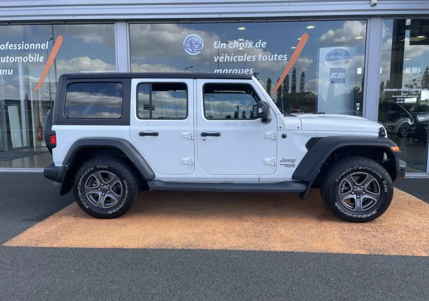 Jeep Wrangler blanc vu de profil côté gauche, avec toit noir et jantes gris foncé sur fond de vitrine commerciale.