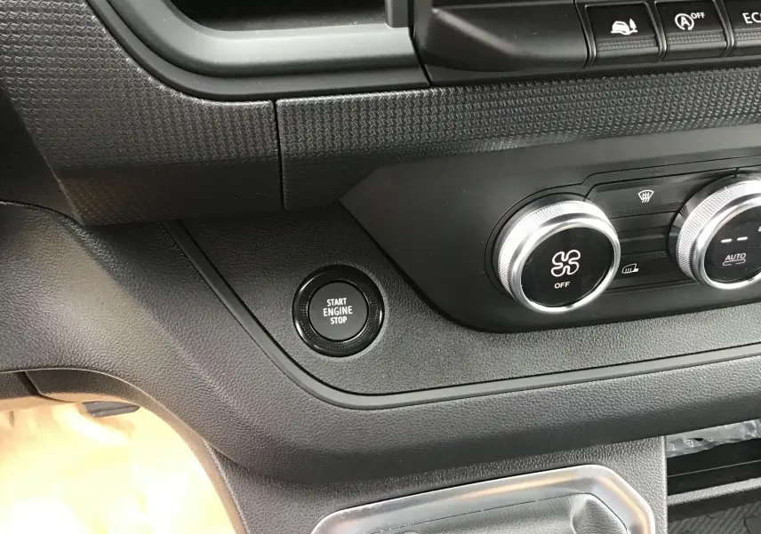 Détail du tableau de bord du Renault Trafic Fourgon noir 2025, avec bouton start/stop et commandes de climatisation.