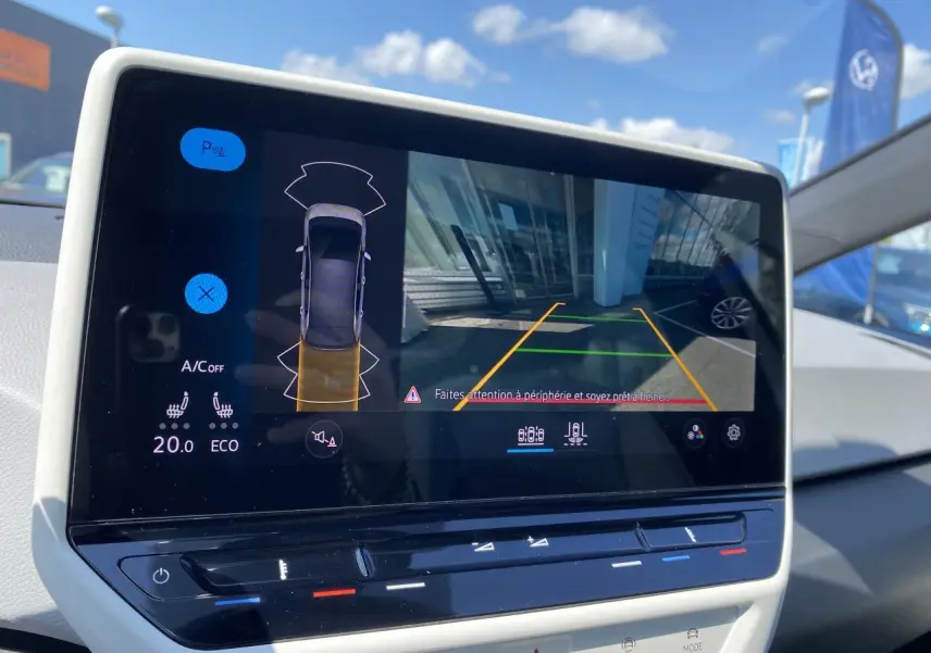 Écran central du Volkswagen ID.3 blanc montrant la caméra de recul et l'aide au stationnement en extérieur.