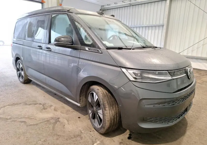 Vue 3/4 avant d’un Volkswagen California T7 gris Indium avec jantes alliage noir brillant et toit relevable fermé.