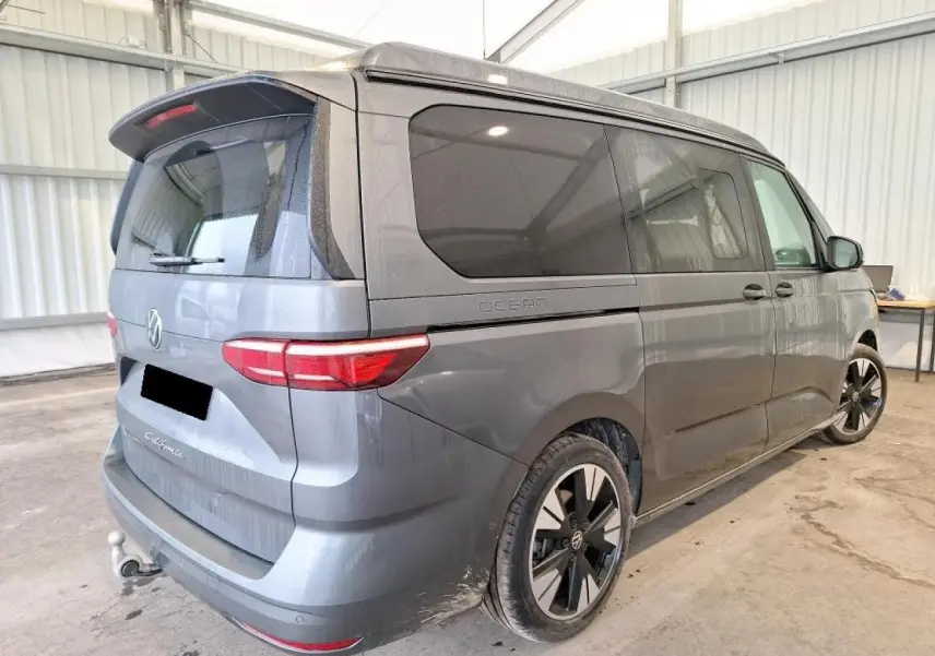 Vue 3/4 arrière droite du Volkswagen California T7 2.0 TDI gris Indium avec jantes alliage noir brillant et attelage rabattable.