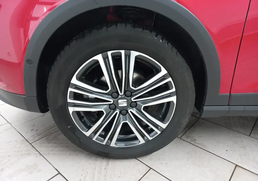Gros plan sur la roue avant gauche d’un SEAT Arona rouge Désir avec jante alliage bicolore et entourage noir.