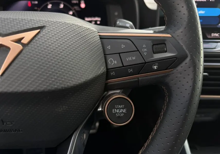 Détail du volant perforé noir avec logo CUPRA cuivre et bouton start/stop sur la droite, intérieur moderne.