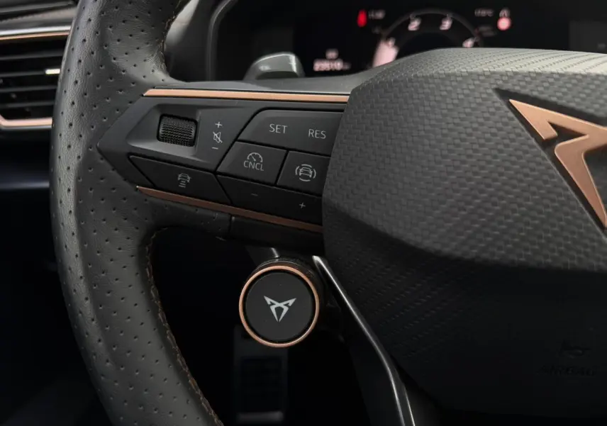 Gros plan sur le volant cuir perforé noir du CUPRA Formentor avec commandes intégrées et logo cuivre distinctif.