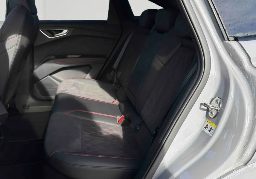 Vue intérieure côté arrière droit de l'Audi Q4 e-tron gris galet, montrant les sièges arrière en tissu noir avec surpiqûres rouges.