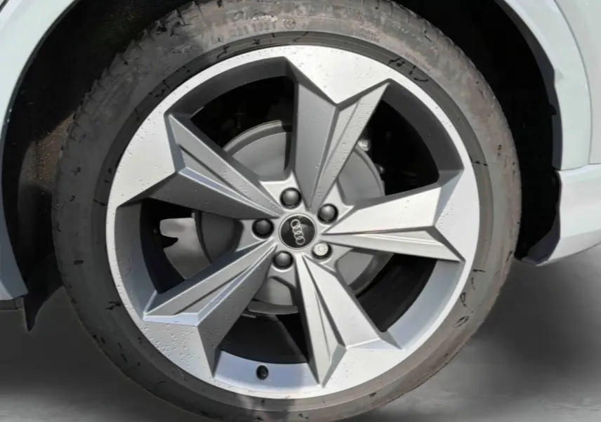 Gros plan sur la jante 19 pouces à 5 bras en étoile de l'Audi Q4 e-tron gris galet, avec logo Audi au centre.