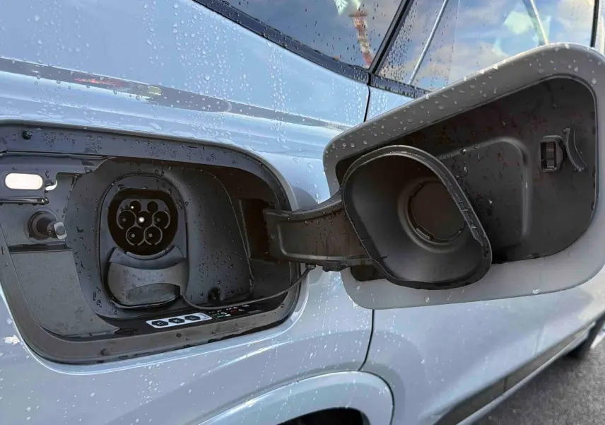 Prise de recharge ouverte côté gauche d’un Audi Q4 e-tron gris galet avec gouttes d’eau sur la carrosserie.