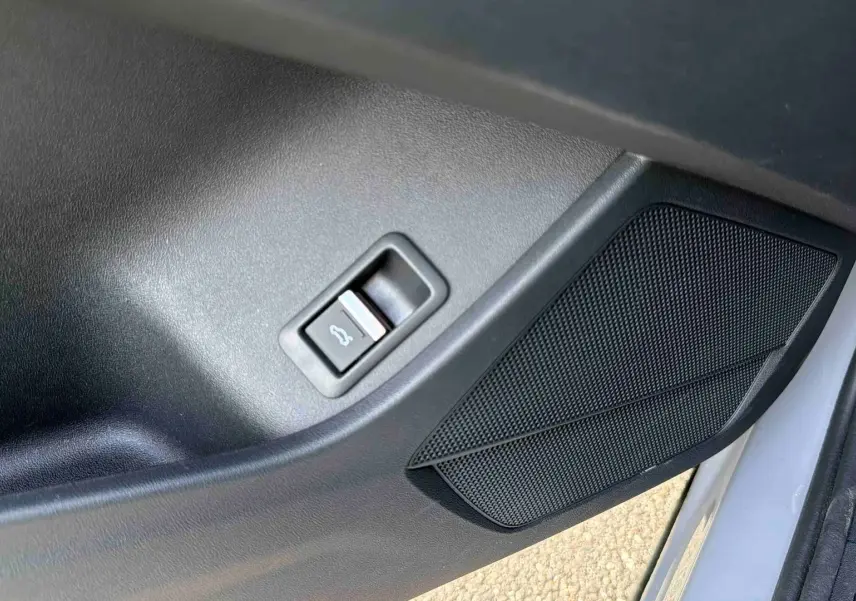 Détail de la porte côté conducteur de l’Audi Q4 e-tron gris galet avec bouton d’ouverture du coffre et haut-parleur intégré.