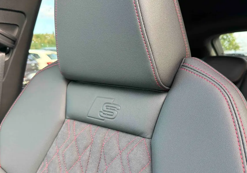 Gros plan sur le siège avant gris foncé avec surpiqûres rouges et logo S embossé, intérieur Audi Q4 e-tron 2025.