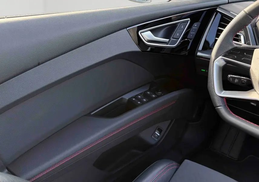 Détail intérieur côté gauche de la porte avant avec surpiqûres rouges et commandes de vitres sur Audi Q4 e-tron.