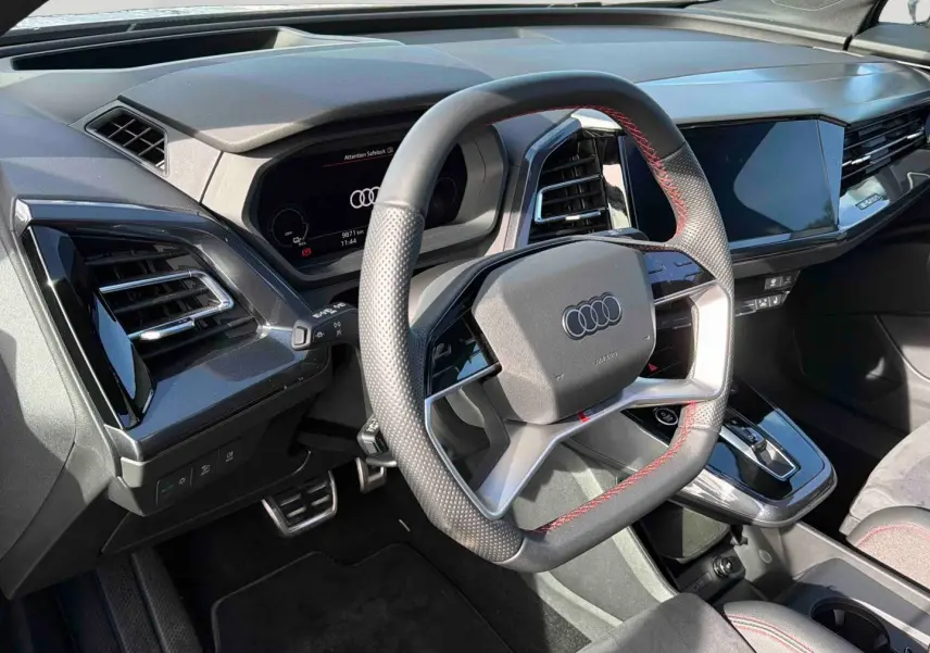 Vue intérieure du volant multifonction noir avec surpiqûres rouges et tableau de bord digital de l'Audi Q4 e-tron 2025.