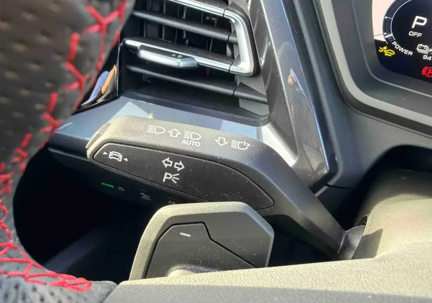 Gros plan sur la commande de clignotants à gauche du volant avec surpiqûres rouges dans un Audi Q4 e-tron gris galet.