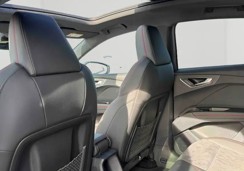 Vue intérieure arrière droite de l'Audi Q4 e-tron 2025 avec sièges en cuir noir et surpiqûres rouges, toit ouvrant panoramique.