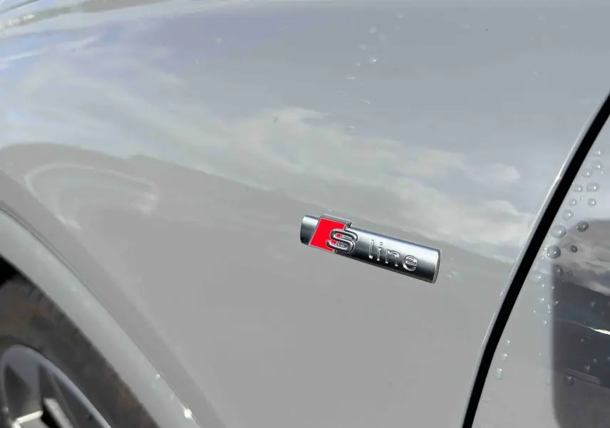 Gros plan sur l'aile avant droite gris galet d'un Audi Q4 e-tron avec logo S line et jante visible.