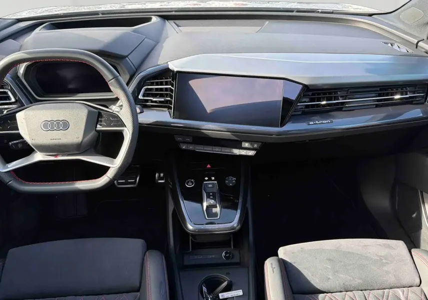 Intérieur Audi Q4 e-tron 2025 vu de face, tableau de bord moderne noir avec écran tactile et volant multifonction cuir.