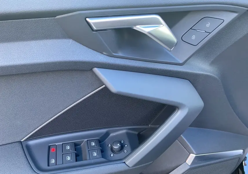 Détail de la porte côté conducteur d'une Audi A3 Sportback noire, montrant les commandes de vitres et de verrouillage.