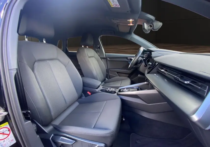 Vue intérieure côté conducteur de l'Audi A3 Sportback 2021 noire, montrant sièges tissu noir et tableau de bord moderne.