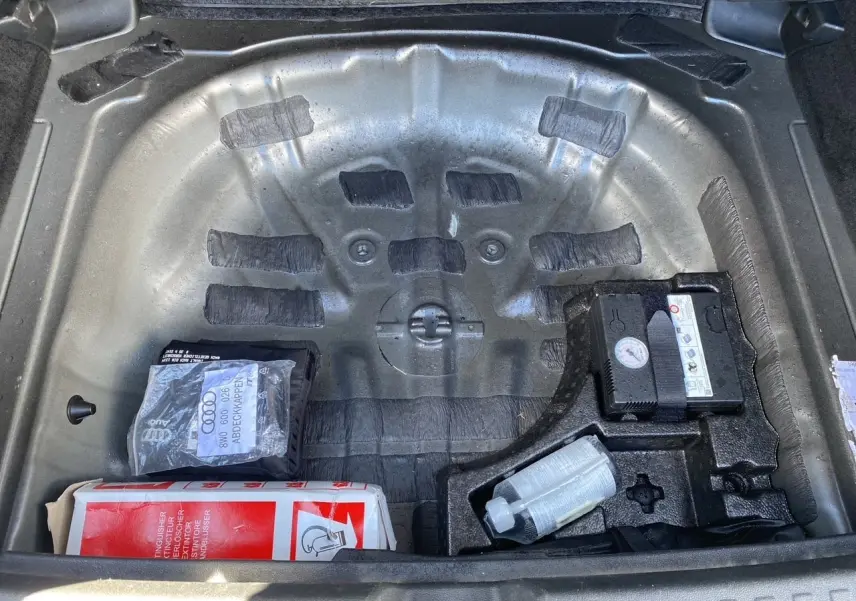Coffre ouvert d'une Audi A3 Sportback noire, vue plongeante sur le compartiment de roue de secours avec kit de réparation.