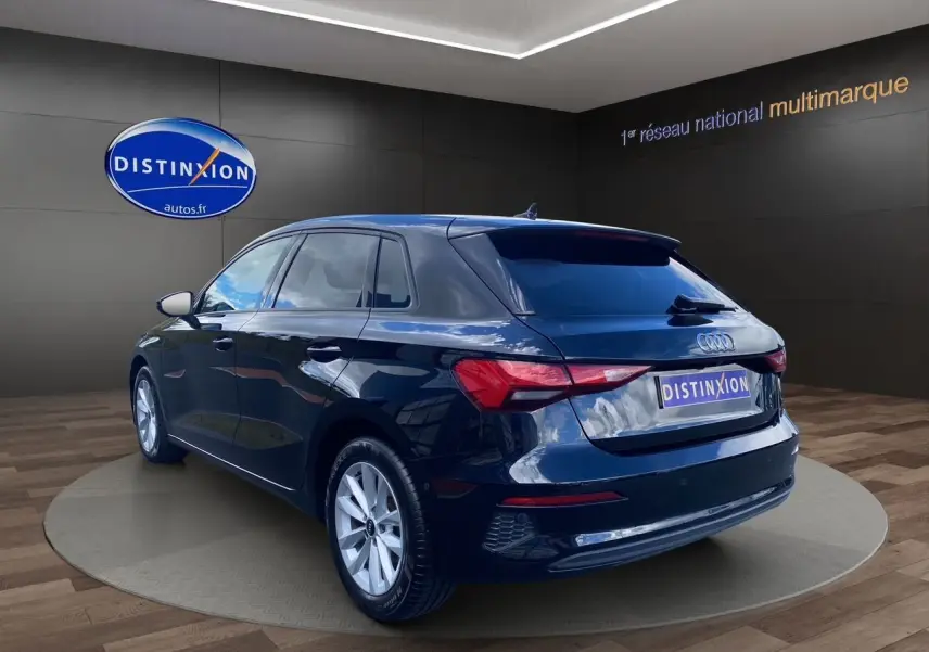 Audi A3 Sportback noir vue 3/4 arrière droit en intérieur avec logo Distinxion sur fond sombre