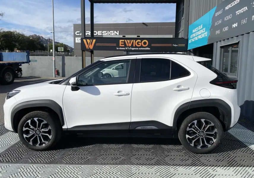 Profil côté gauche de la Toyota Yaris Cross blanche pure 2025 avec jantes alliage et toit noir contrasté.