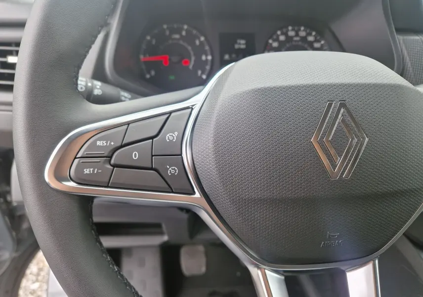 Gros plan sur le volant noir du Renault Trafic Fourgon 2025, avec commandes intégrées et logo Renault central argenté.