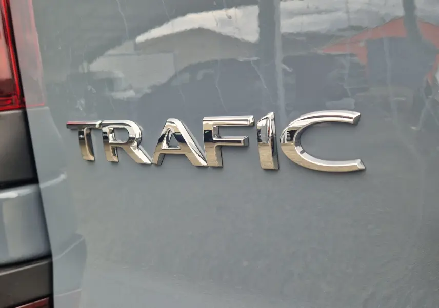 Gros plan sur l’inscription TRAFIC en chrome sur la porte arrière d’un Renault Trafic gris urbain.