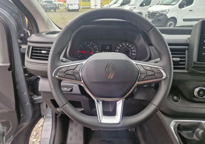 Vue intérieure centrée sur le volant du Renault Trafic Fourgon gris urbain 2025 avec commandes intégrées et tableau de bord visible.