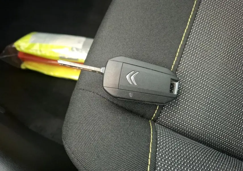 Clé noire Citroën posée sur un siège tissu gris foncé avec surpiqûres jaunes, intérieur du véhicule visible en arrière-plan.