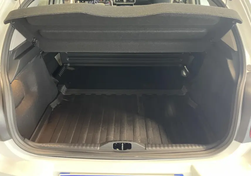 Coffre ouvert vu de l'arrière d'une Citroën C3 blanche 2023, avec tapis de coffre noir et cache-bagages relevé.