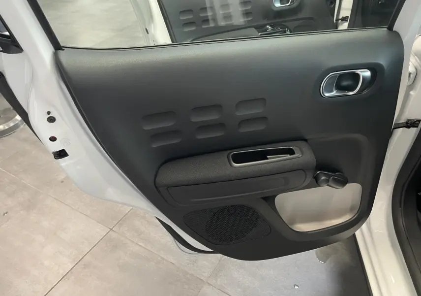 Vue rapprochée de la porte arrière gauche noire avec manivelle sur une Citroën C3 blanche 2023.
