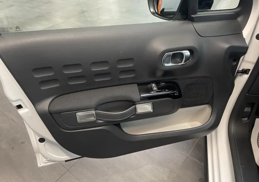 Vue intérieure de la porte avant gauche blanche de la Citroën C3 2023 avec poignée textile et commandes électriques.