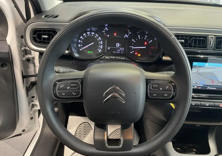 Vue intérieure centrée sur le volant noir de la Citroën C3 blanche, avec tableau de bord et écran tactile visibles.